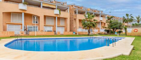 A residential building with a swimming pool, balconies, and palm trees.