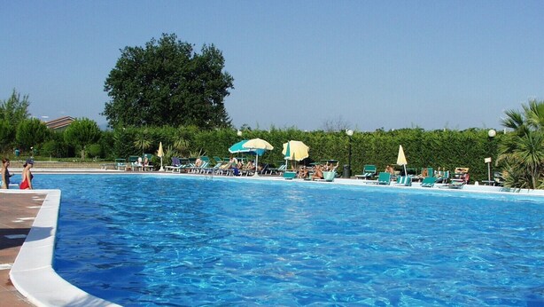 A large outdoor swimming pool with lounge chairs and umbrellas, surrounded by greenery.