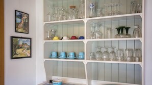 A dining area with a white table, blue plates, and glassware on shelves.