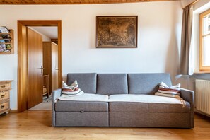 A grey sofa with pillows, a wooden door, a framed picture, and a window with curtains. - Holiday Apartment 'Haus Thurn Apartment B' with Mountain View, Garden & Wi-Fi (Kastelruth)