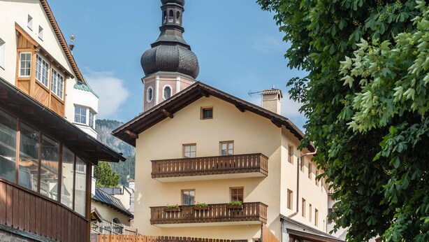 A building with a prominent tower, balconies with railings, and a mountain backdrop. - Holiday Apartment 'Haus Thurn Apartment B' with Mountain View, Garden & Wi-Fi (Kastelruth)