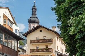A building with a prominent tower, balconies with railings, and a mountain backdrop.