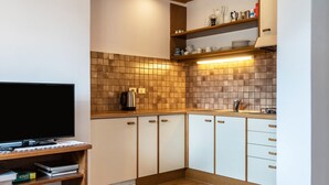 A compact kitchen with a TV, wooden cabinets, and a tiled backsplash. - Holiday Apartment 'Haus Thurn Apartment B' with Mountain View, Garden & Wi-Fi (Kastelruth)