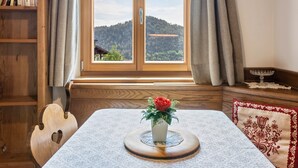 A room with a wooden bookshelf, a table with a white tablecloth, a vase with a red flower, and a window with a view of a hill. - Holiday Apartment 'Haus Thurn Apartment B' with Mountain View, Garden & Wi-Fi (Kastelruth)