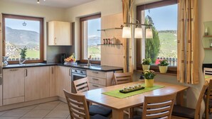 Une cuisine moderne avec des meubles en bois, une table à manger, des chaises, une vue sur la campagne et une fenêtre avec des rideaux.