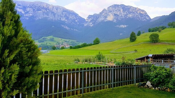 Un paysage rural avec une clôture en bois, des champs verdoyants et une chaîne de montagnes en arrière-plan.