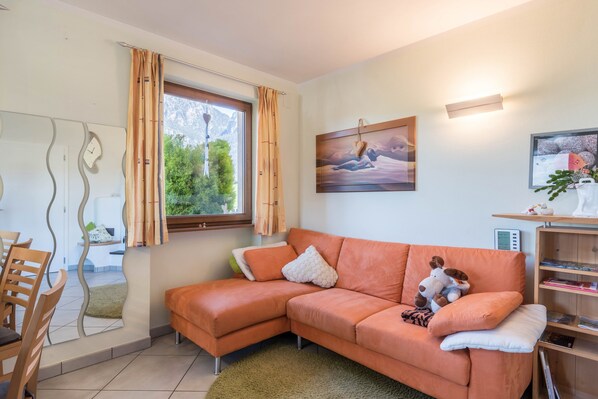 Een moderne woonkamer met een hoekbank, een eethoek met stoelen, een raam met gordijnen en een schilderij aan de muur.