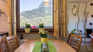 Une table à manger avec des chaises, une fenêtre avec des rideaux et des plantes en pot sur un rebord de fenêtre.
