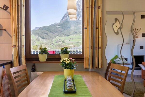 Une table à manger avec des chaises, une fenêtre avec des rideaux et des plantes en pot sur un rebord de fenêtre.