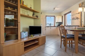 Een moderne keuken met houten kastjes, een eethoek met een tafel en stoelen, en een televisie op een houten dressoir.