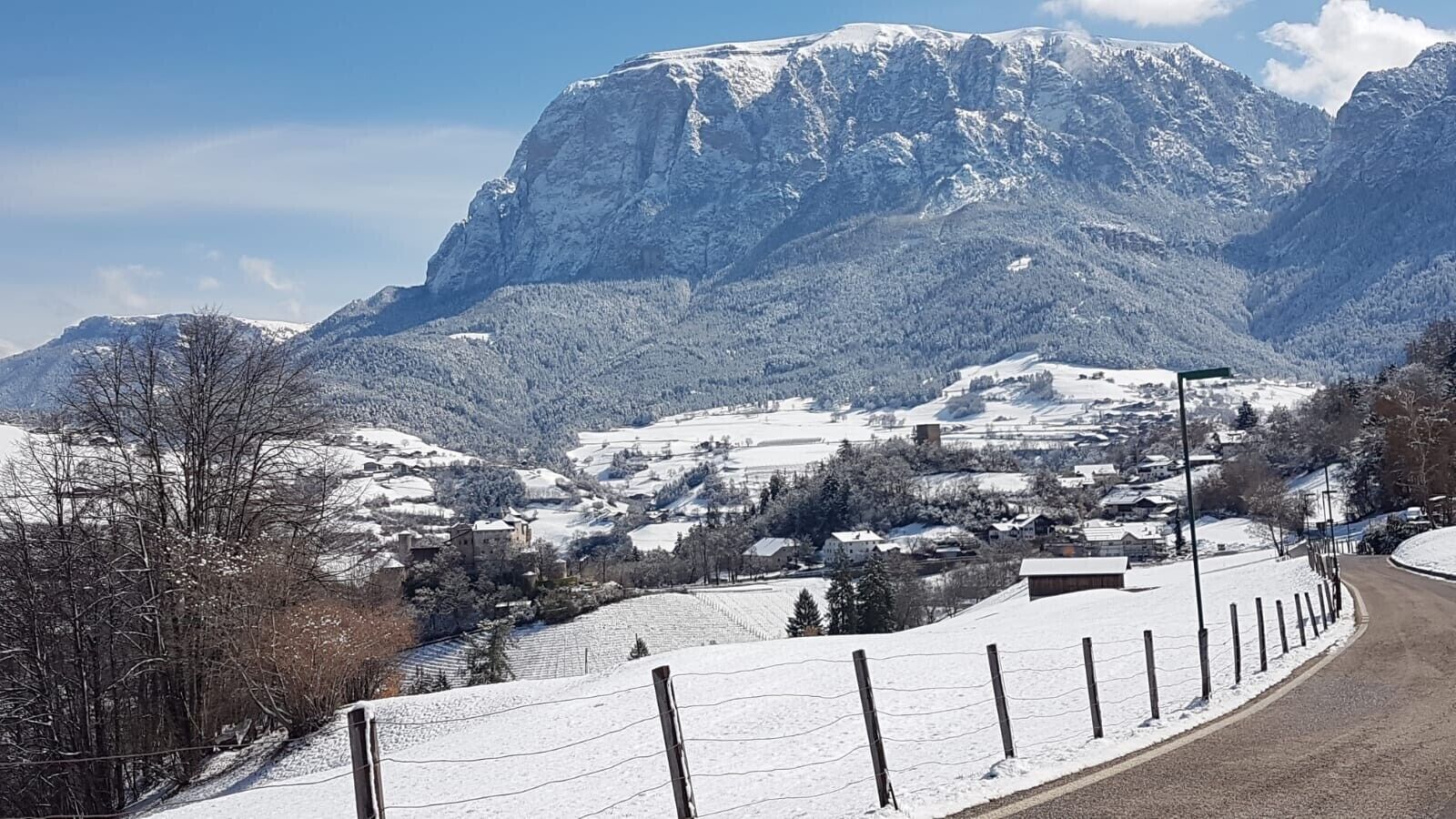 Eine verschneite Landschaft mit einem Berg, einer Straße und einem Zaun.
