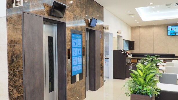 A modern hotel lobby with marble walls, an elevator, a reception desk, and a seating area with a potted plant. - Toyoko Inn Yokohama Shiei-chikatetsu Center Minami-eki (Yokohama)