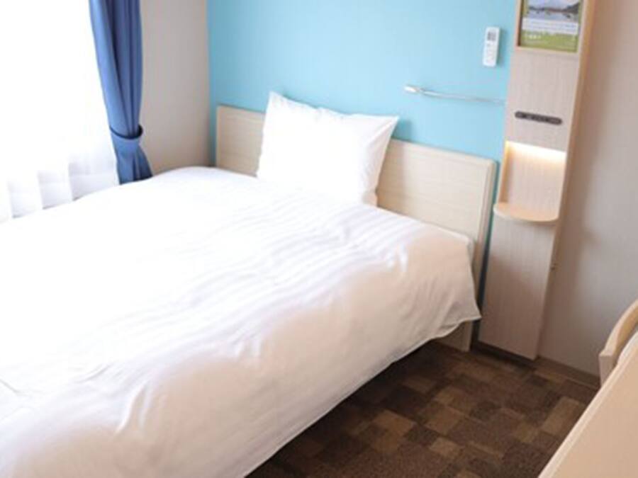 Un lit bien fait dans une chambre d’hôtel, avec un sol à carreaux, un mur bleu et une armoire en bois avec une lampe.