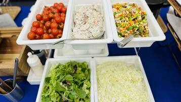 Une table de buffet proposant divers plats, notamment des tomates cerises, une salade crémeuse, un mélange de légumes, une salade verte et du fromage râpé.
