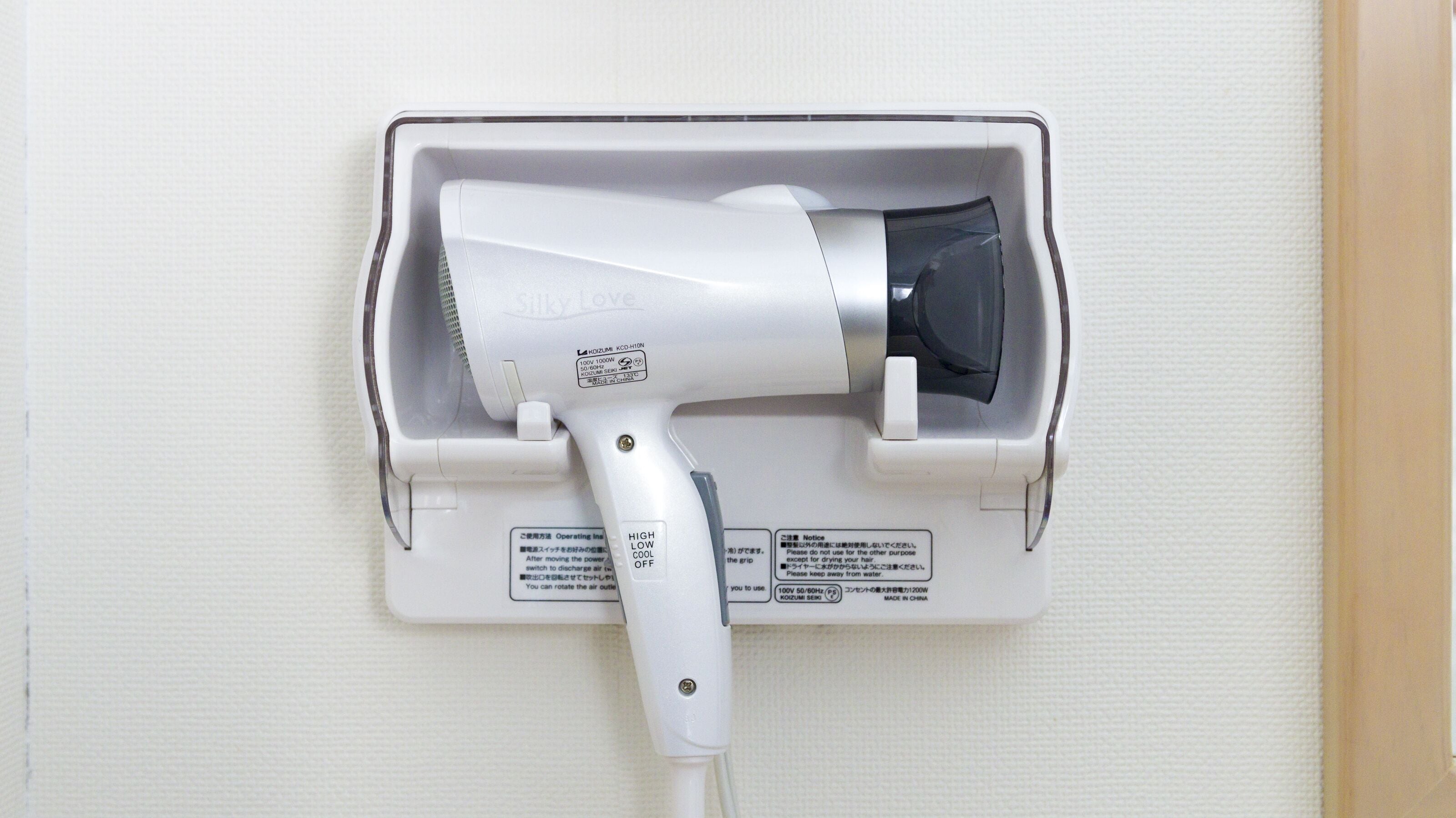 A hair dryer mounted on a wall with a power outlet and a switch.