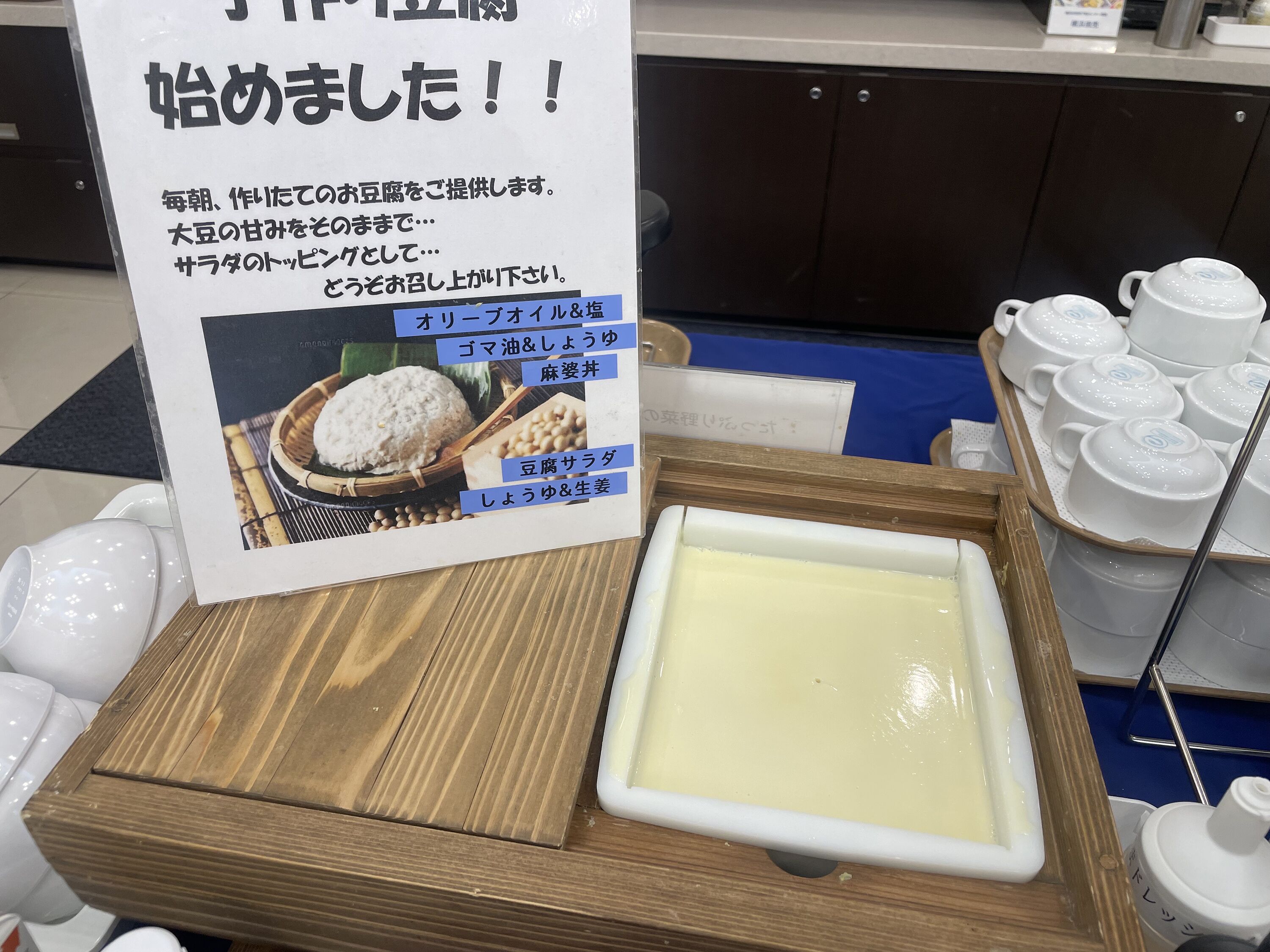 A display of Japanese food items including rice, soybeans, and a white dish, possibly a dessert, on a wooden tray.