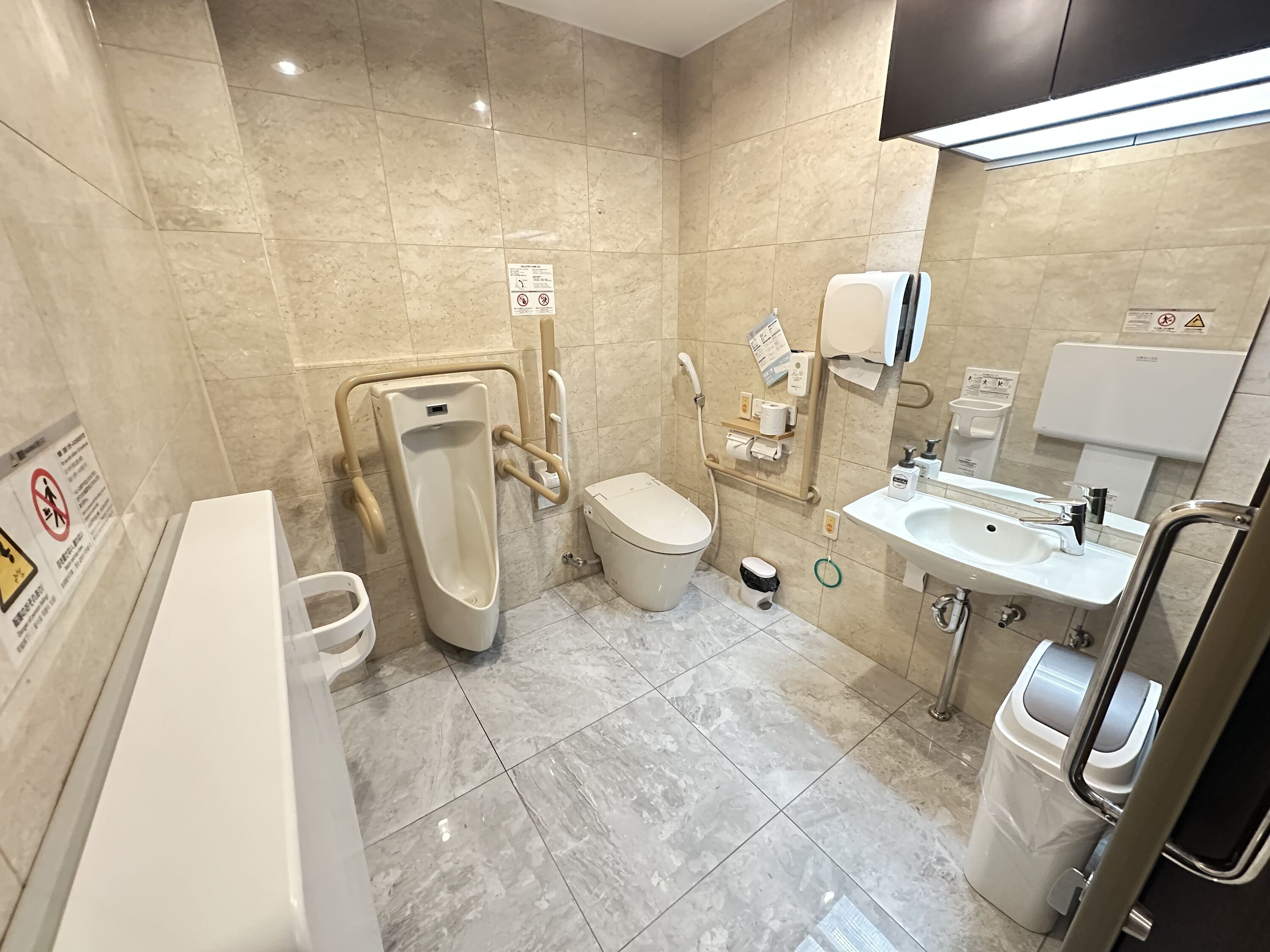 A modern bathroom with a urinal, toilet, sink, and hand dryer.