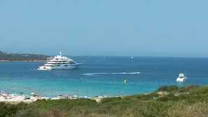 Eine große Yacht ankert in der Nähe eines Strandes mit klarem, blauem Wasser und ein paar kleineren Booten in der Ferne.