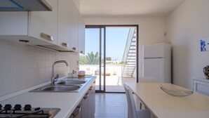 A modern kitchen with a sink, stove, and refrigerator, leading to a balcony with a view.