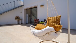 A white wicker swing chair with cushions, a staircase, and a door leading to an interior space.