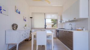 A modern kitchen with white cabinetry, a dining table with chairs, and a window with blinds.