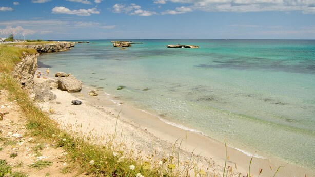 A beach with clear turquoise water, rocky outcrops, and a sandy shore.