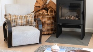 Ett modernt vardagsrum med en svart soffa, en korg av rotting och en svart vedkamin.