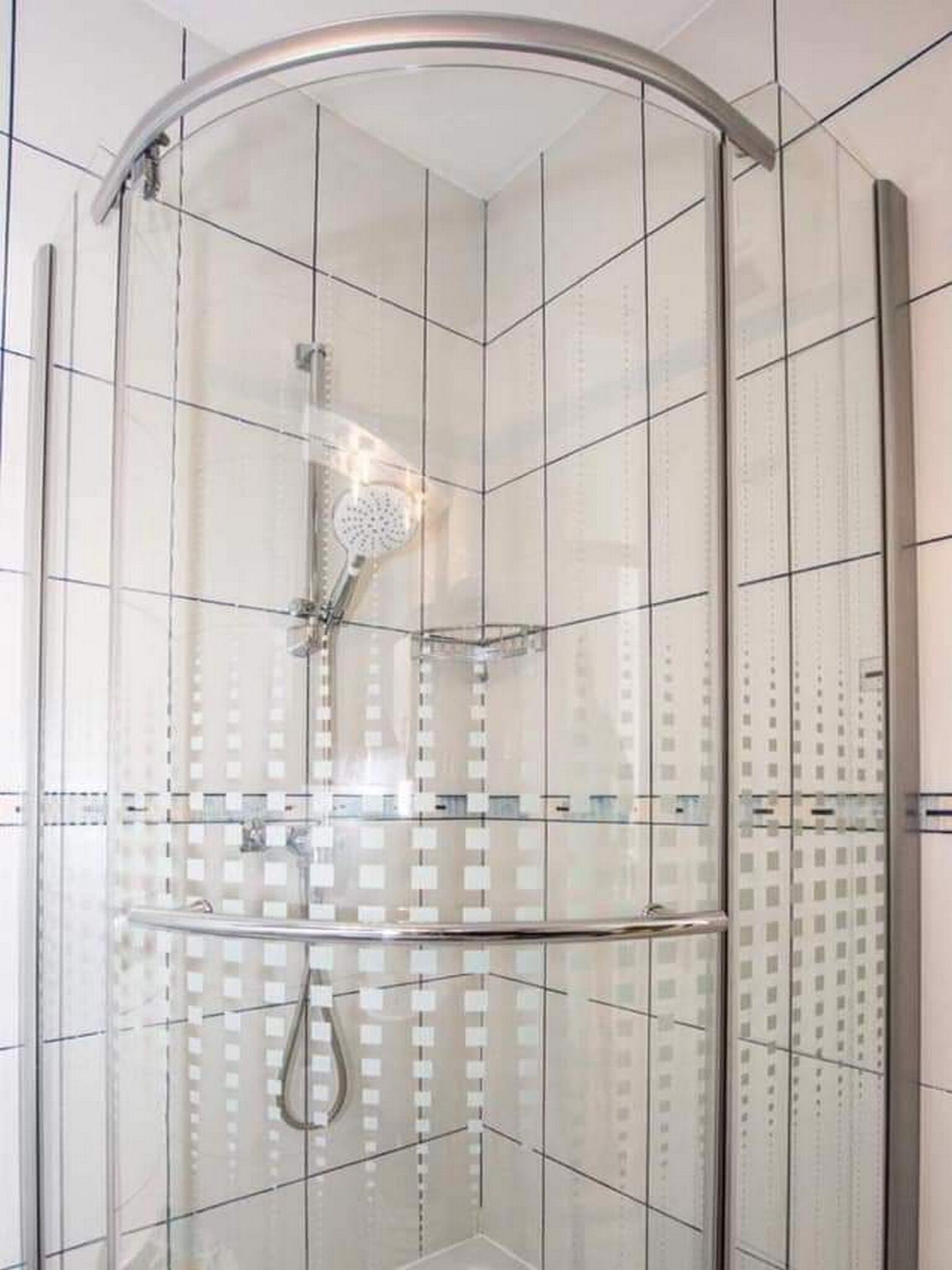 A glass-enclosed shower with a curved door, tiled walls, and a visible showerhead.