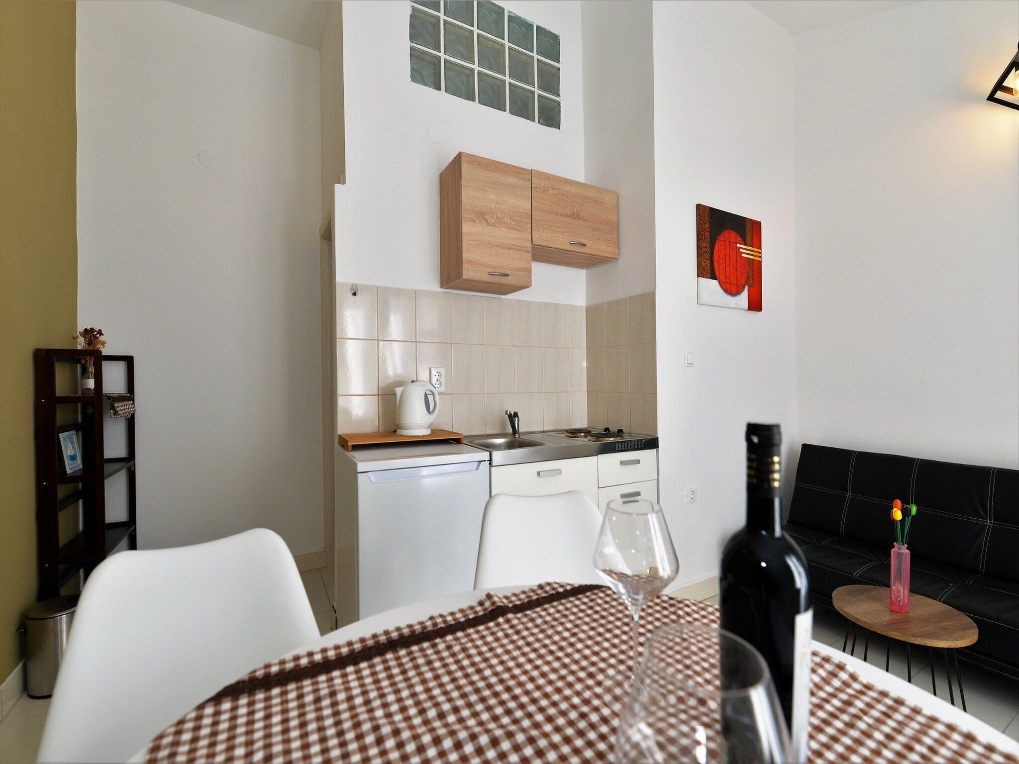 A compact kitchen with white appliances, a wooden cabinet, and a small dining area with a checkered tablecloth.