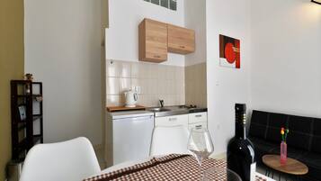 A compact kitchen with white appliances, a wooden cabinet, and a small dining area with a checkered tablecloth.