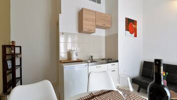 Een compacte keuken met witte kastjes, een houten aanrecht en een klein eetgedeelte met een geruit tafelkleed.