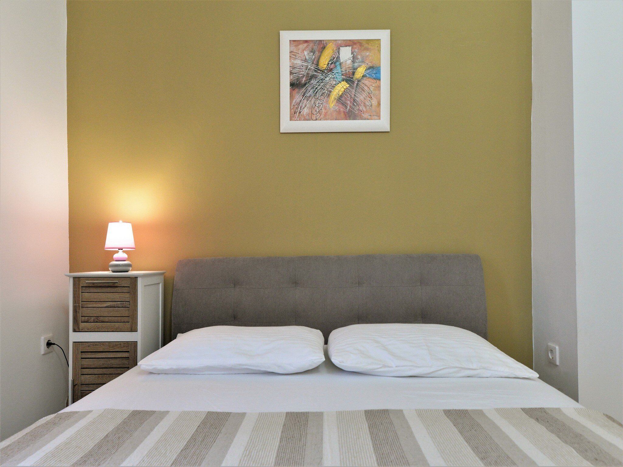 Una cama con dos almohadas, una mesita de noche con una lámpara y un cuadro abstracto enmarcado en la pared.