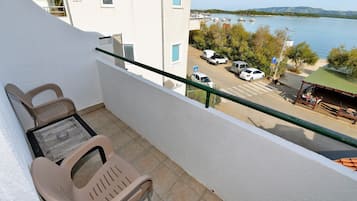 A balcony with two plastic chairs, a table, and a view of a marina with boats and a beach.