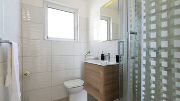 Un baño moderno con inodoro, lavamanos y cabina de ducha con mampara de vidrio.