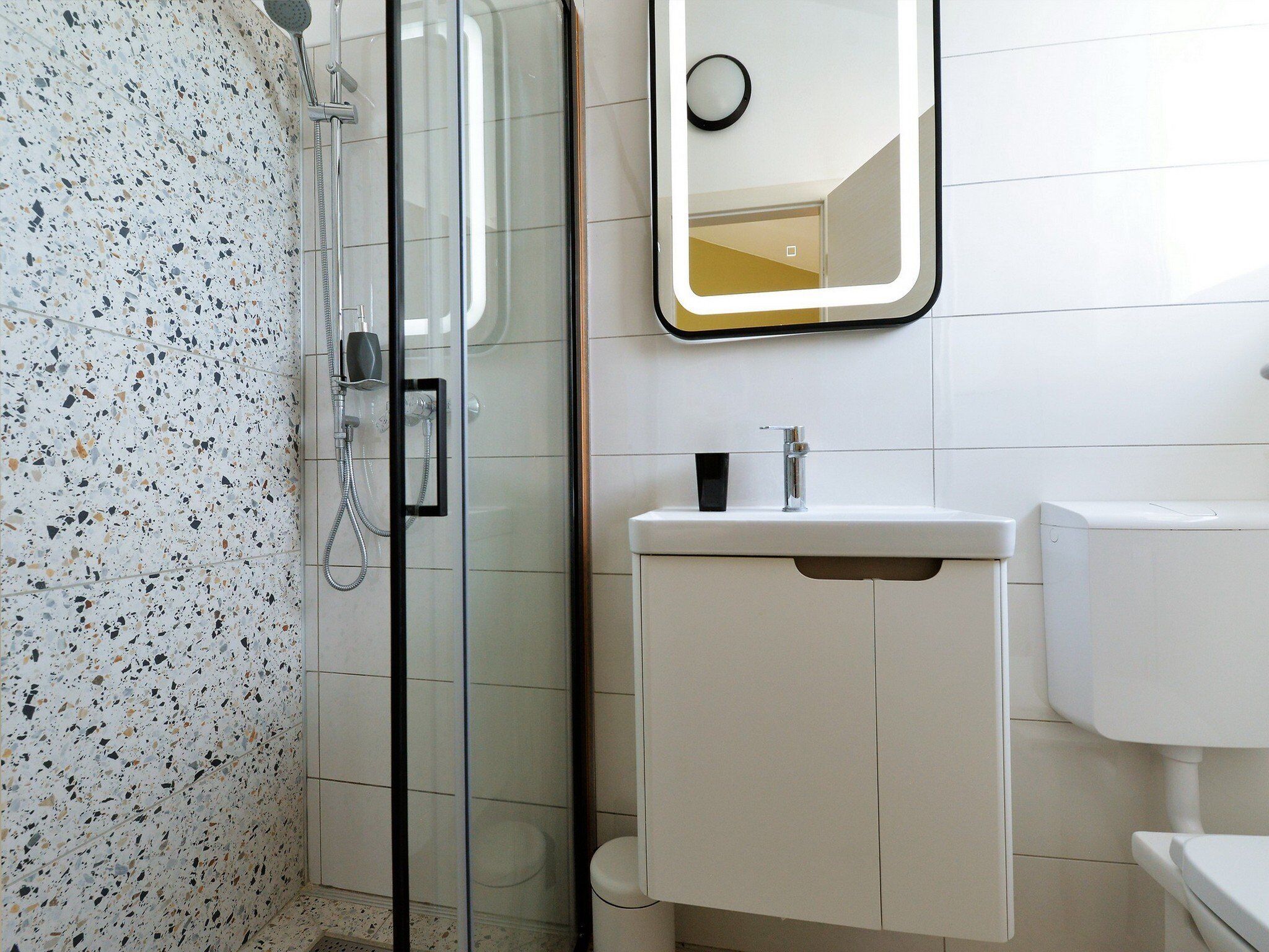 A modern bathroom with a glass-enclosed shower, a white sink, and a toilet.