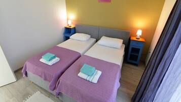 A double room with two beds, each with a purple bedspread and white pillows, and a small bedside table with a lamp.