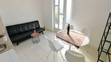 A modern living room with a black sofa, a small round table with a vase of flowers, and a dining table with chairs.