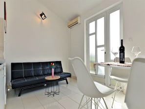 A modern living room with a black leather sofa, a white chair, a small round table, and a dining table with two wine glasses and a bottle. - Apartments Helena (Murter-Kornati)