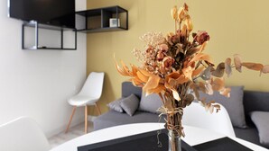 Una sala de estar moderna con un sofá, una silla blanca y un florero con flores secas sobre una mesa.