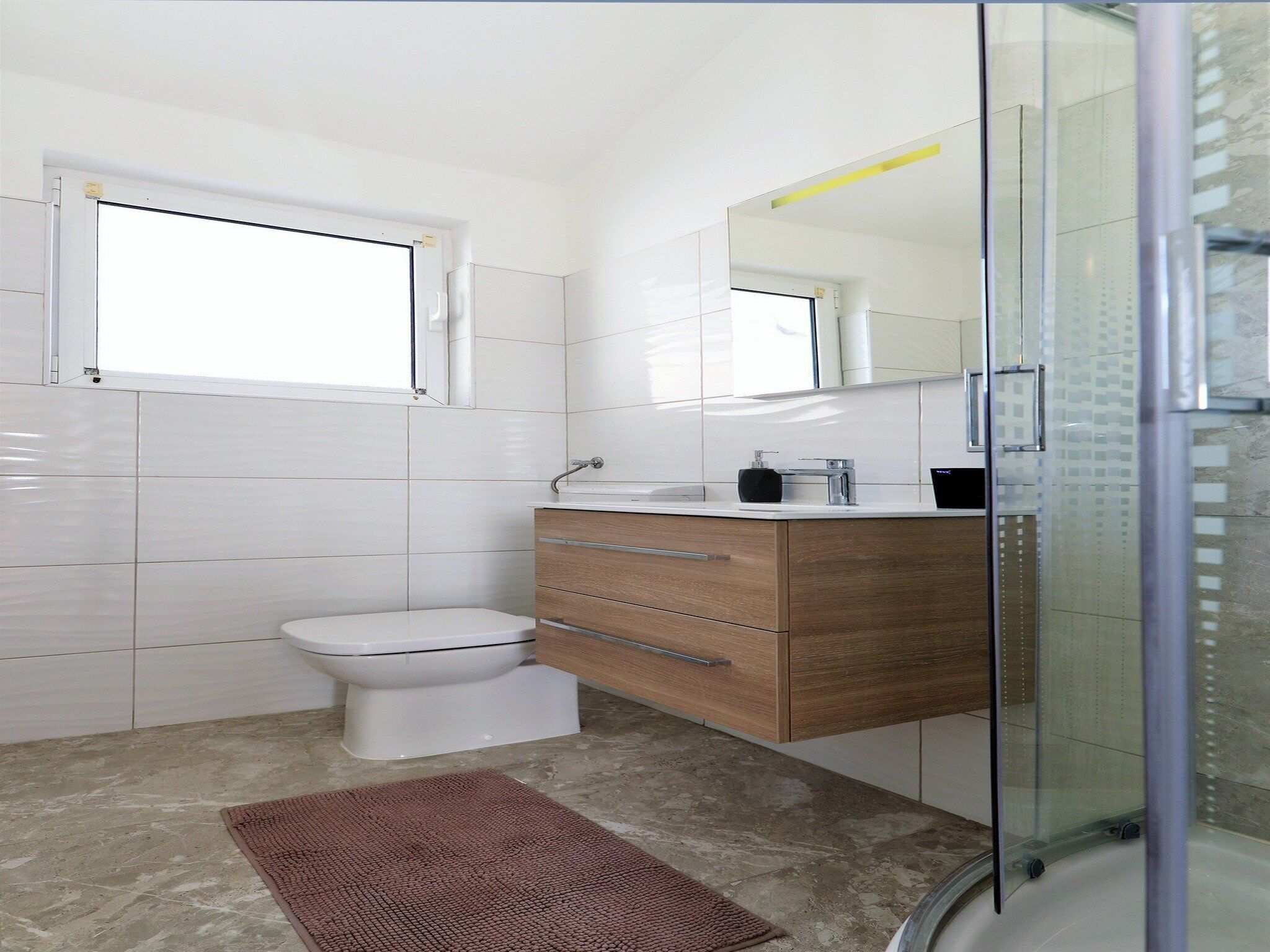Ein modernes Badezimmer mit Toilette, Waschtisch und einer Duschkabine aus Glas.