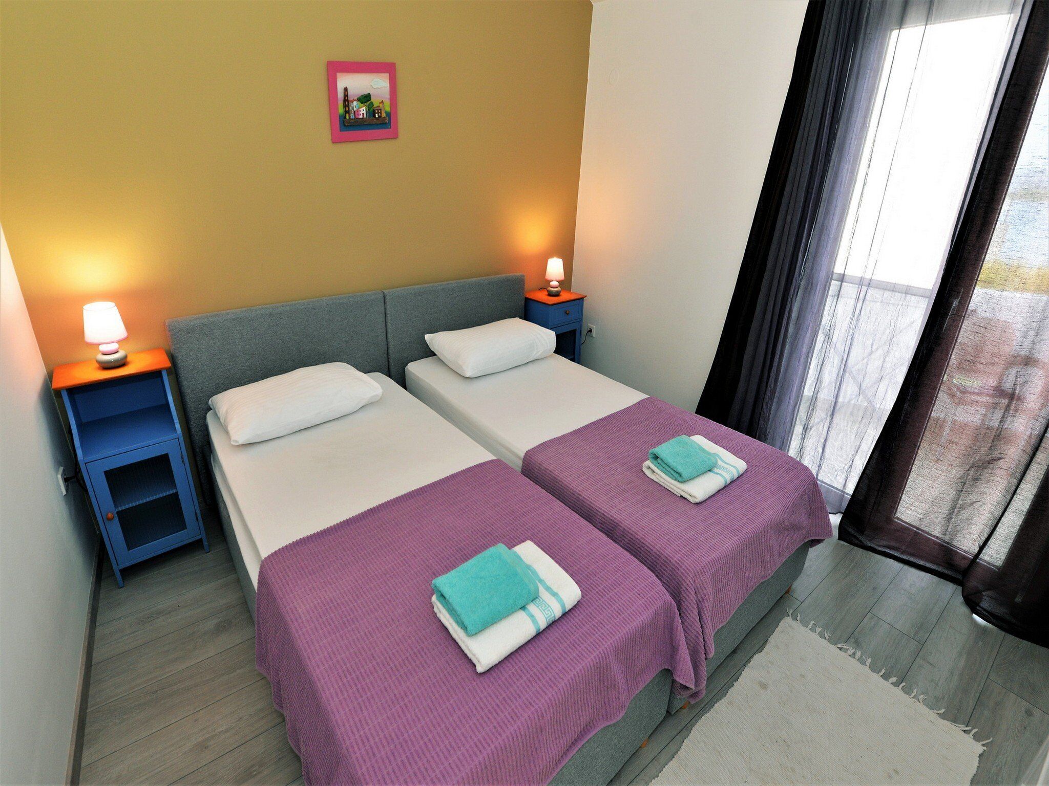 A hotel room with two beds, a nightstand with a lamp, and a picture on the wall.