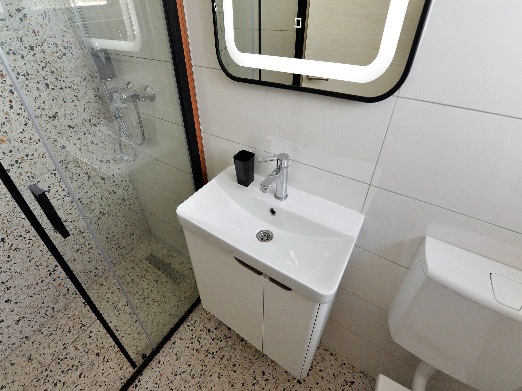 A bathroom with a white sink, a mirror, and a shower enclosure.
