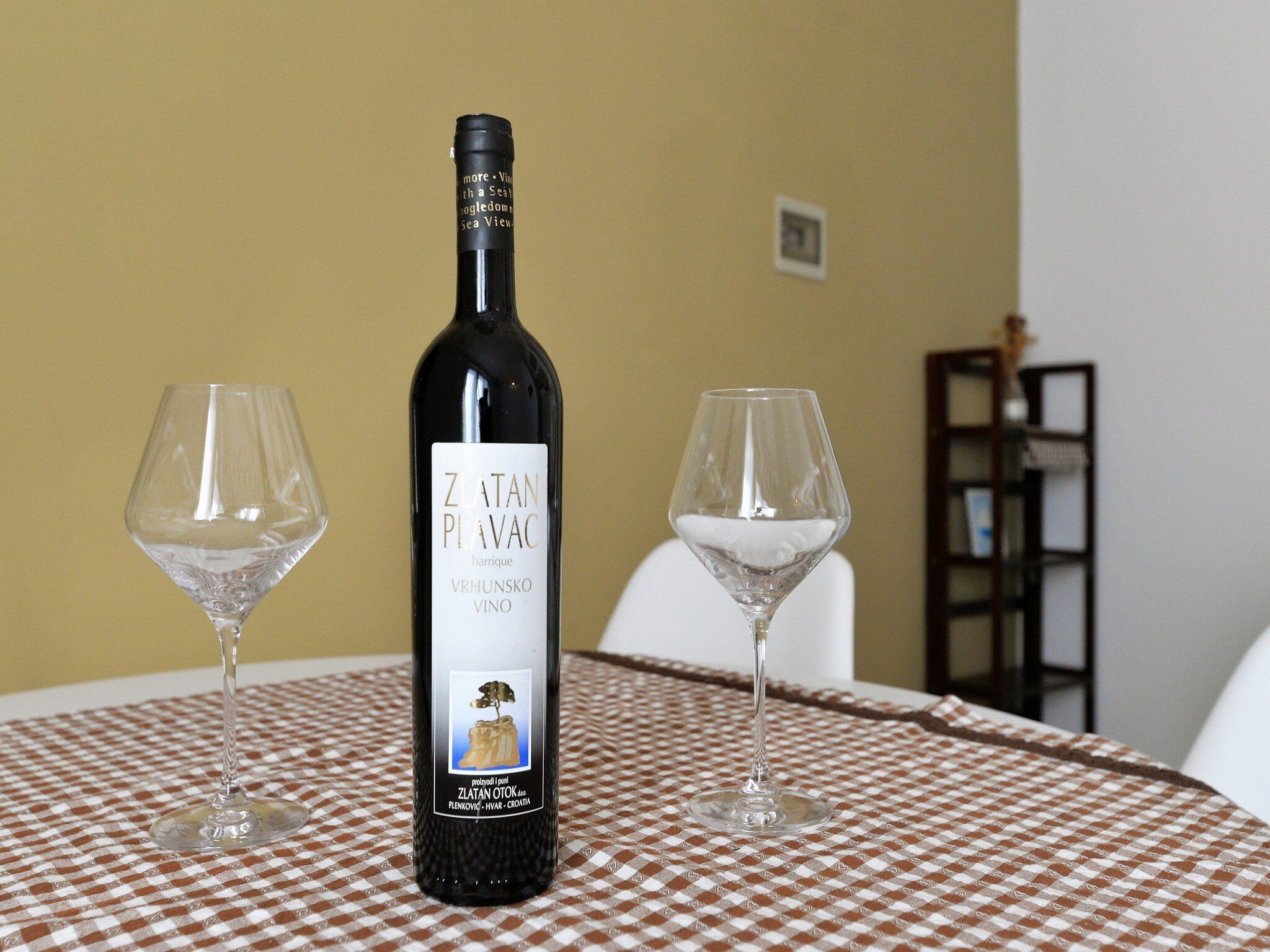 A bottle of Zlatan Plavac wine on a table with two wine glasses.