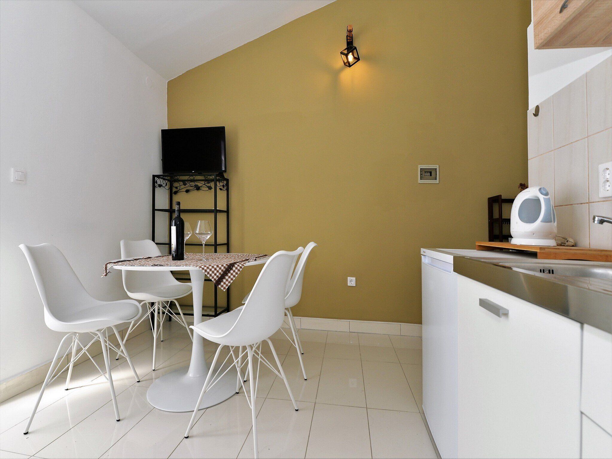 A modern kitchen with white cabinetry, a dining area with white chairs and a table, and a yellow accent wall.
