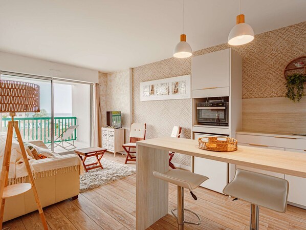 A modern kitchen with a bar area, wooden flooring, and a view of the sea.