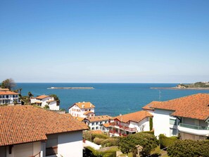 A coastal residential area with houses featuring red-tiled roofs and white walls, overlooking the sea.