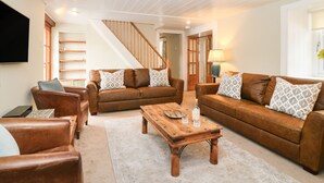 Ein geräumiges Wohnzimmer mit einer Holztreppe, Ledersofas und einem Couchtisch.