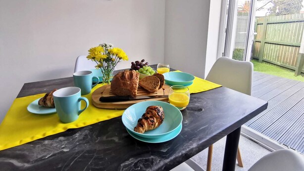 Una mesa de desayuno con pan, croissants y fruta, sobre un mantel amarillo.