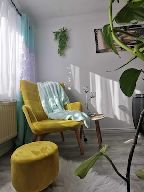 A yellow armchair with a light blue throw blanket, a small round table with a decorative item, a potted plant, and a radiator.