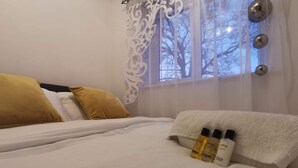 Una cama bien hecha con almohadas blancas y mostaza, una toalla blanca y dos botellas a un lado.